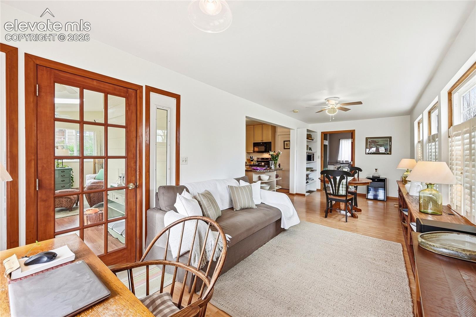 French door entry with multi-pane glass, wood-finish flooring, built-in shelving, and multiple windows with plantation shutters