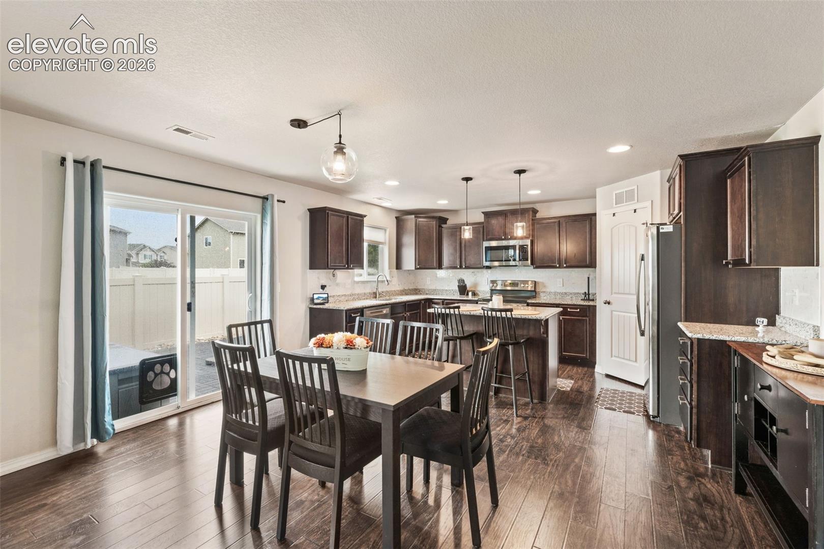 Open-concept kitchen and dining area featuring wood-finish flooring, dark wood cabinetry, light countertops, and stainless steel appliances