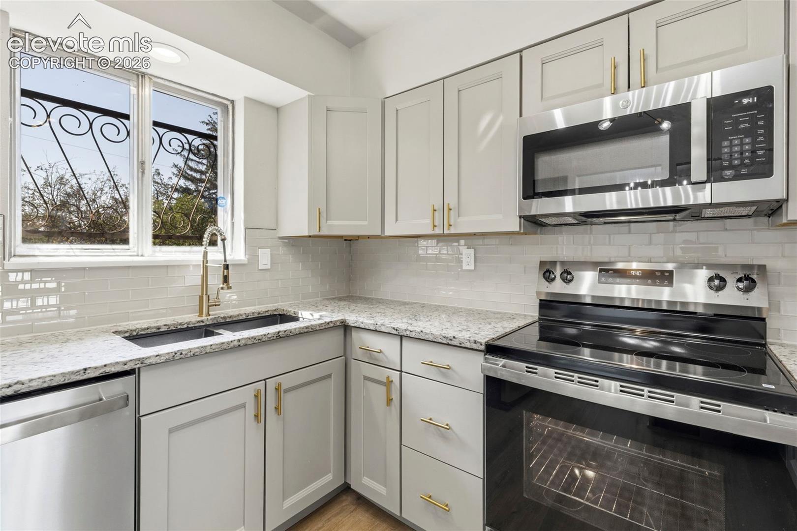 Kitchen featuring light cabinetry, stainless steel appliances, granite-style countertops, and a subway tile backsplash