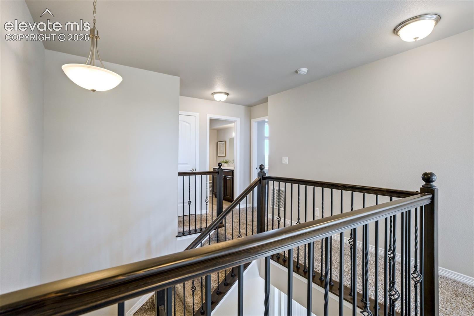 Wrought iron balusters, dark wood handrail, recessed ceiling lighting, pendant light fixture, and textured carpeted flooring