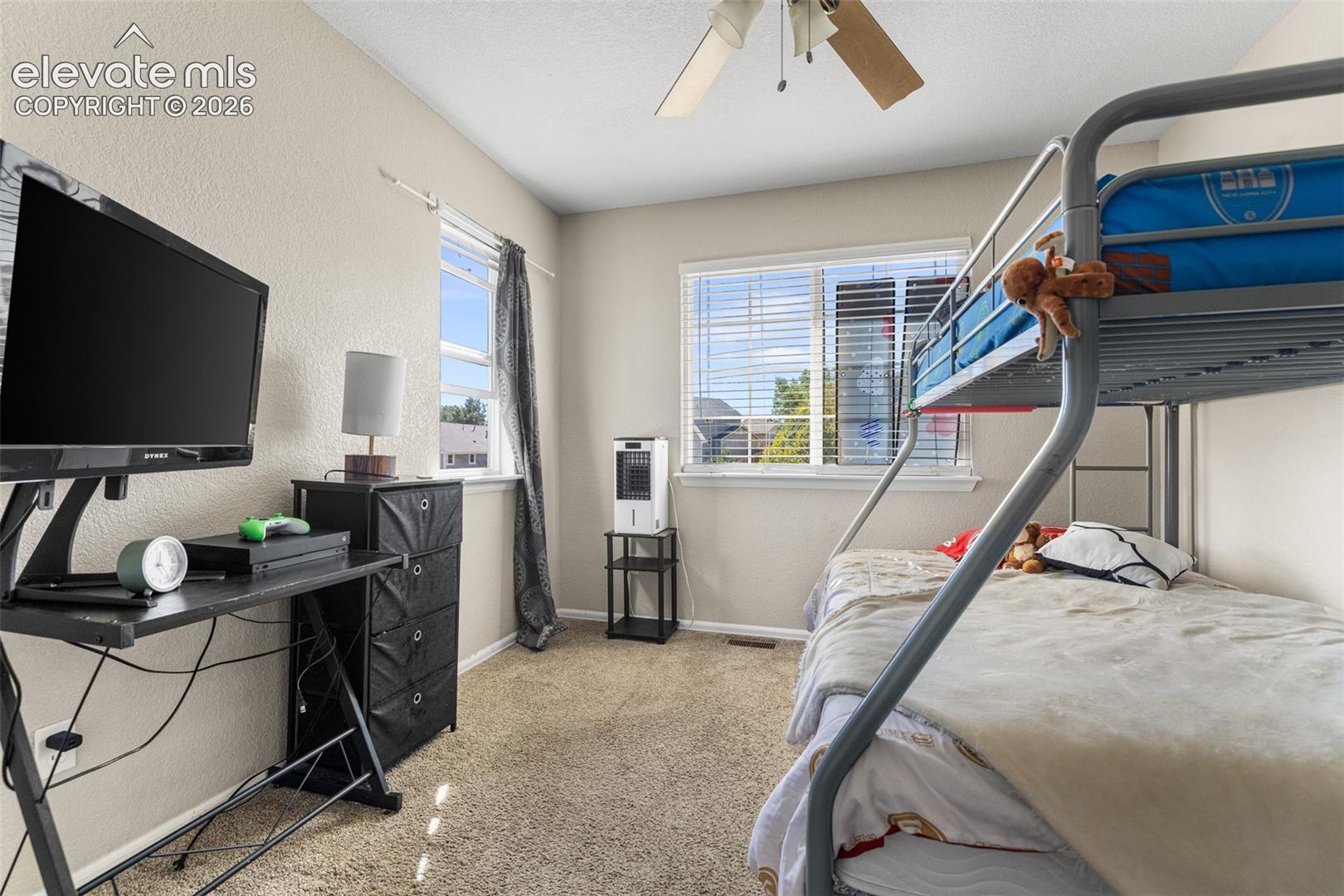 Bedroom featuring neutral wall-to-wall carpeting, dual windows with horizontal blinds, and a ceiling-mounted fan with light fixture