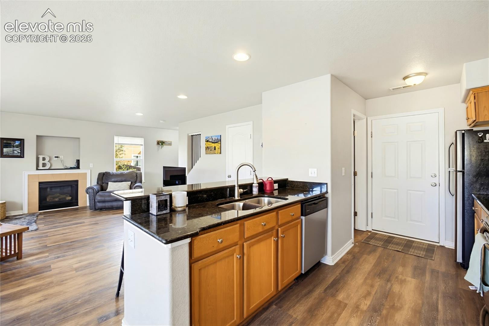 Kitchen featuring a stone-surface breakfast bar, wood cabinetry, stainless steel sink, and recessed lighting, paired with wood-finish flooring and a fireplace with a built-in recessed niche