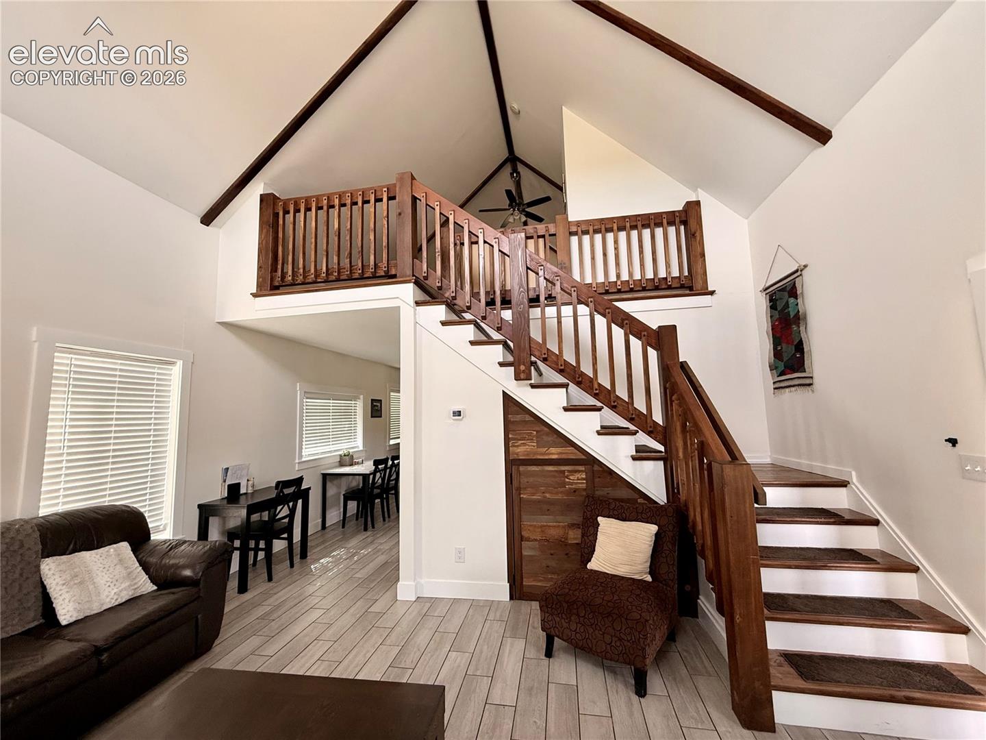 Soaring vaulted ceilings with exposed beams, wood-finish flooring, and a prominent staircase with wood railing