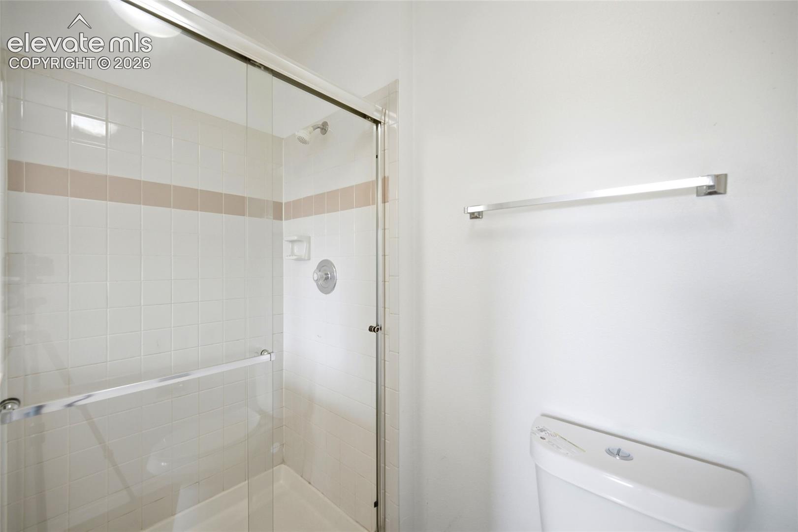 Shower enclosure featuring a chrome-framed glass door, white wall tiling with a decorative accent row, integrated soap niche, wall-mounted chrome shower fixture, and a chrome towel bar