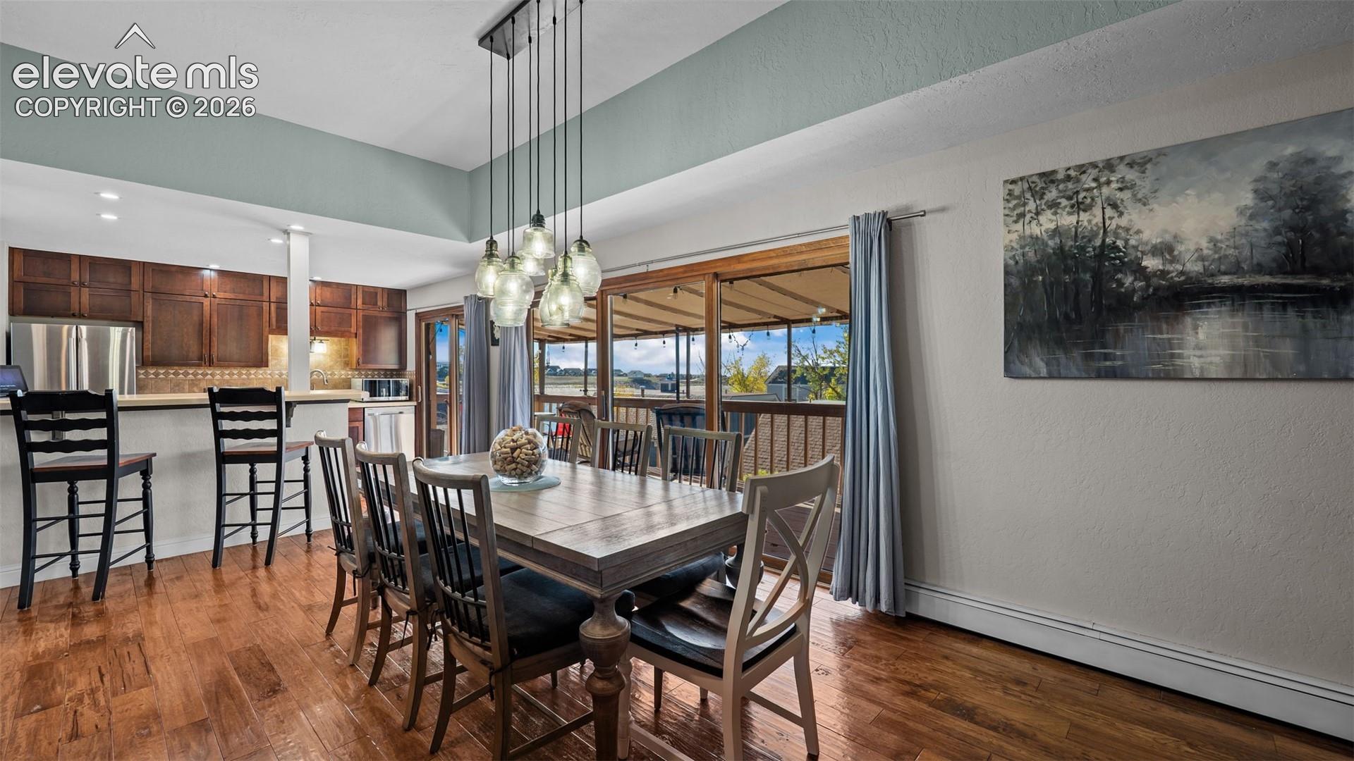 Dining area featuring wood-finish flooring, a multi-pendant light fixture, and a tray ceiling, paired with kitchen cabinetry and sliding glass doors leading to a deck
