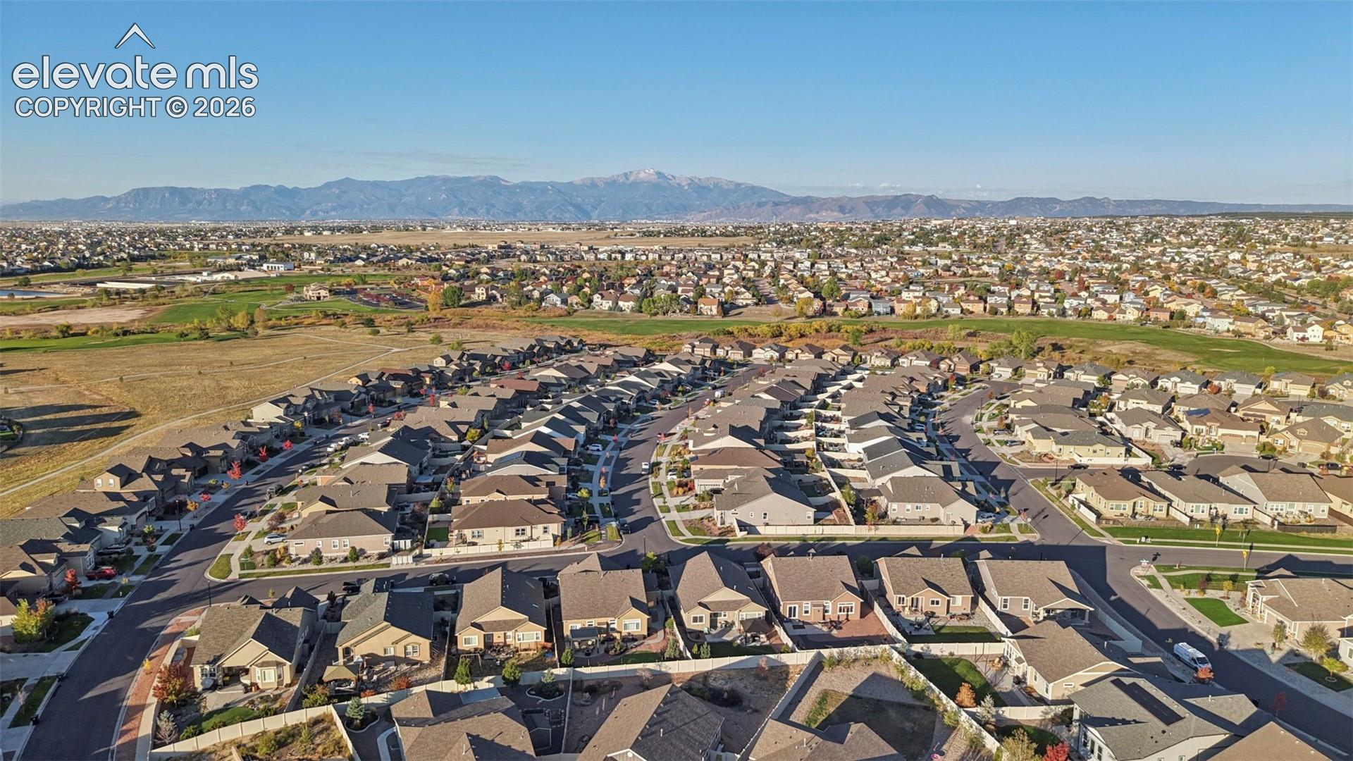 Expansive residential area with multiple single-family homes, clear mountain backdrop, and surrounding open fields