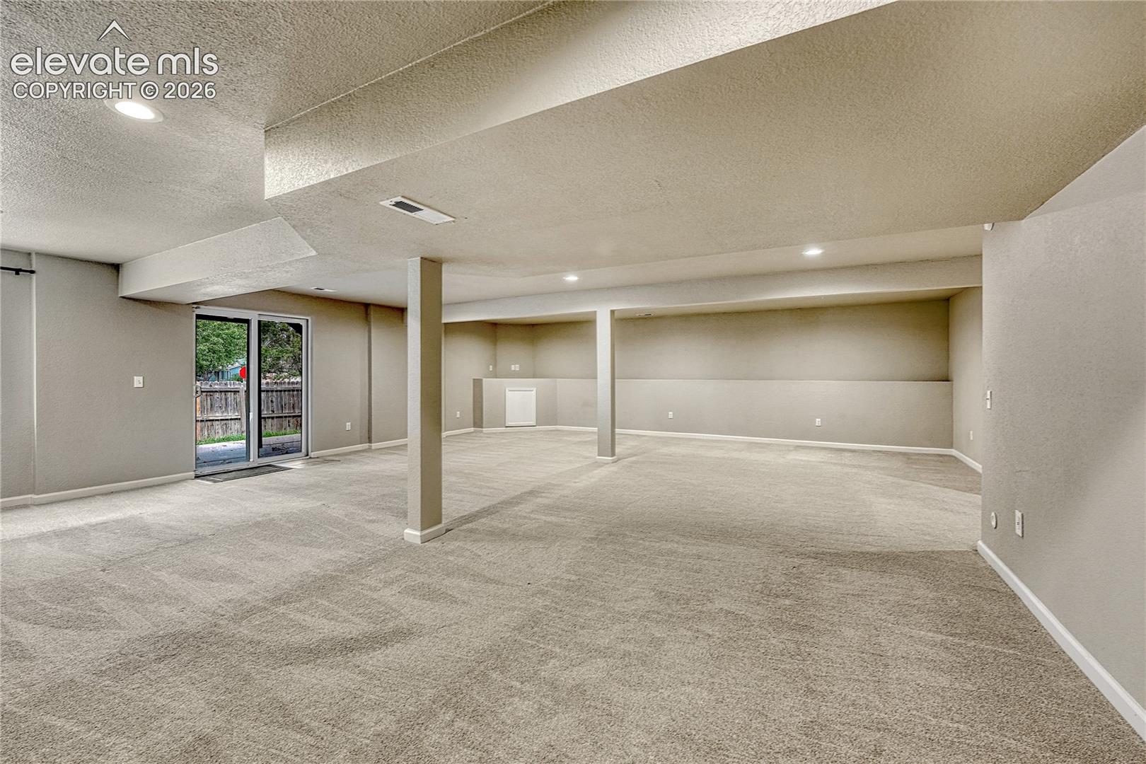 Expansive interior space featuring neutral wall tones, wall-to-wall carpeting, recessed ceiling lighting, and a sliding glass door providing exterior access