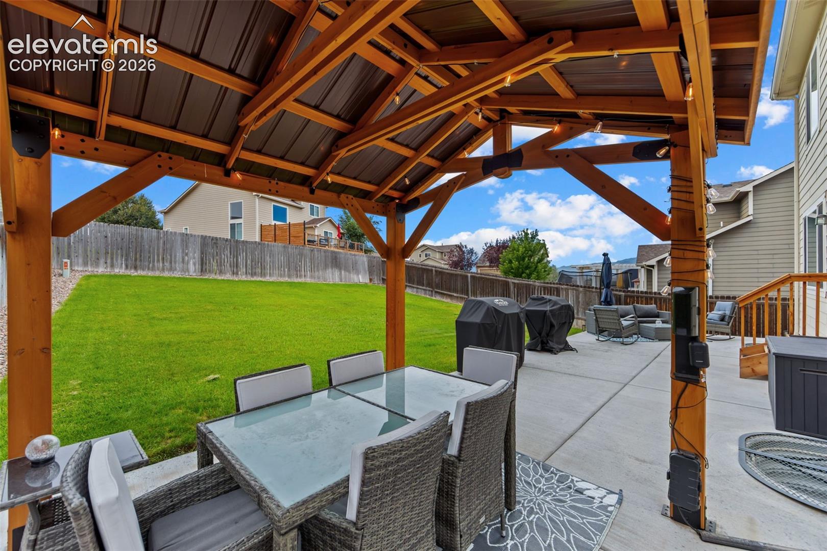 Expansive backyard featuring a covered patio with wood beam construction, a concrete patio, and a manicured lawn