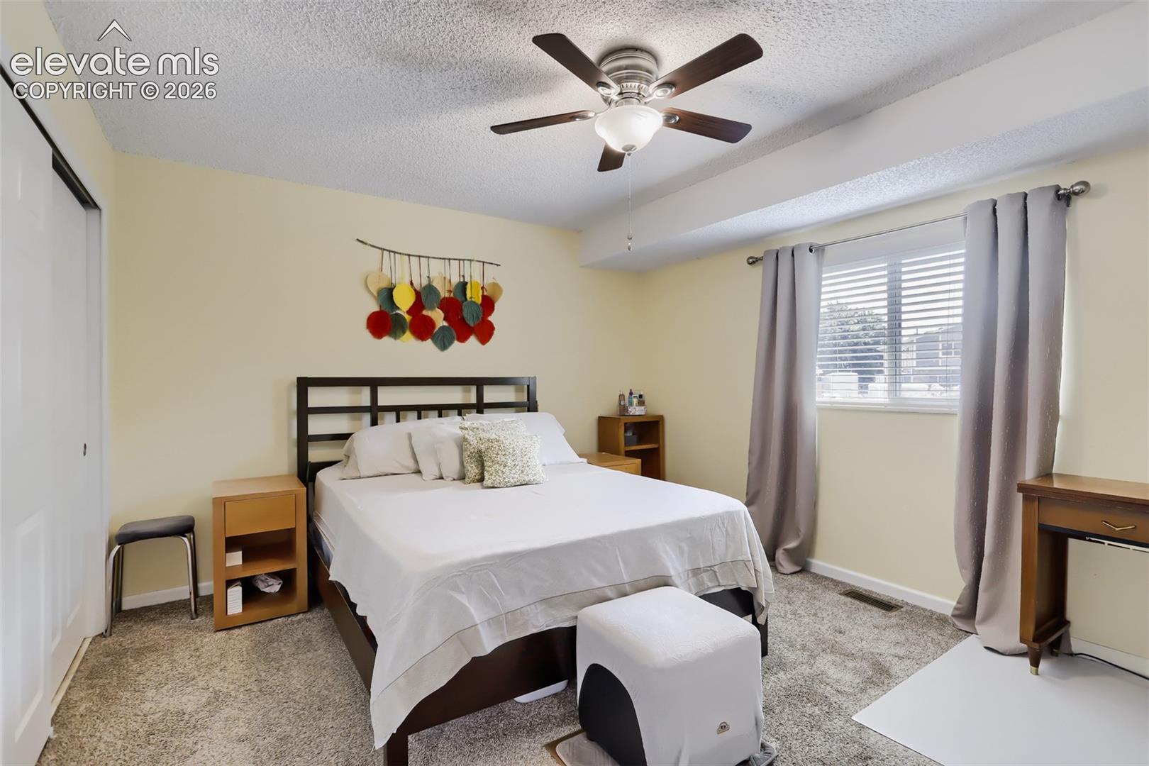Bedroom featuring carpet flooring, a ceiling fan with light fixture, and a window with blinds and curtains