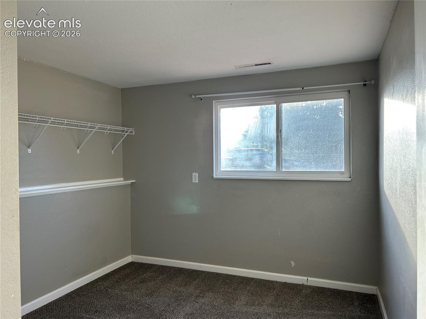 Neutral interior featuring gray walls, carpeted flooring, a sliding window with a horizontal rod, and wall-mounted wire shelving