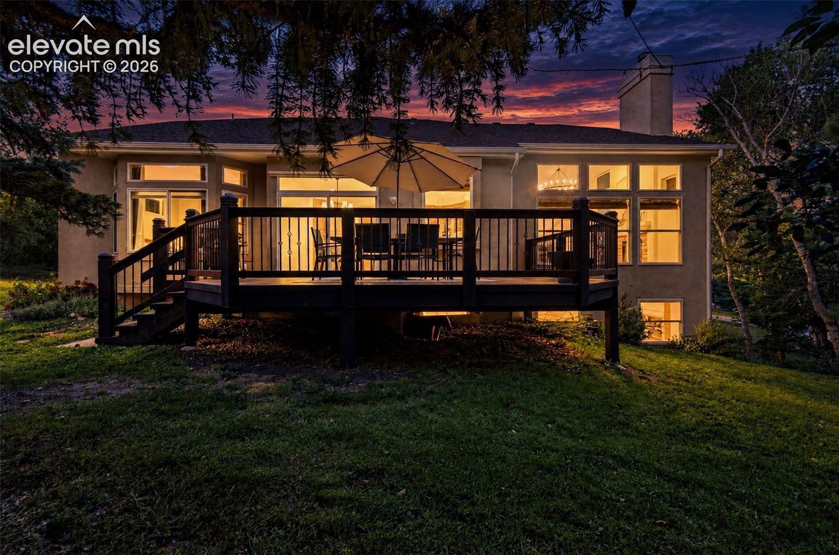 Expansive rear deck with dark wood-finish railing, ground-level access, multiple sliding glass doors, and a prominent chimney