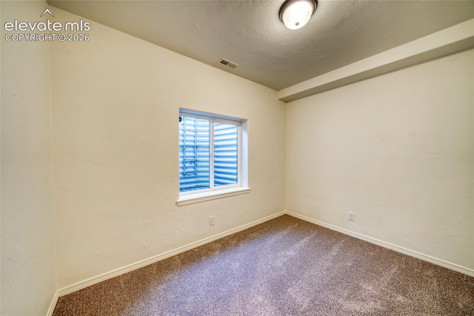 Carpeted room with a single window and overhead flush-mount lighting