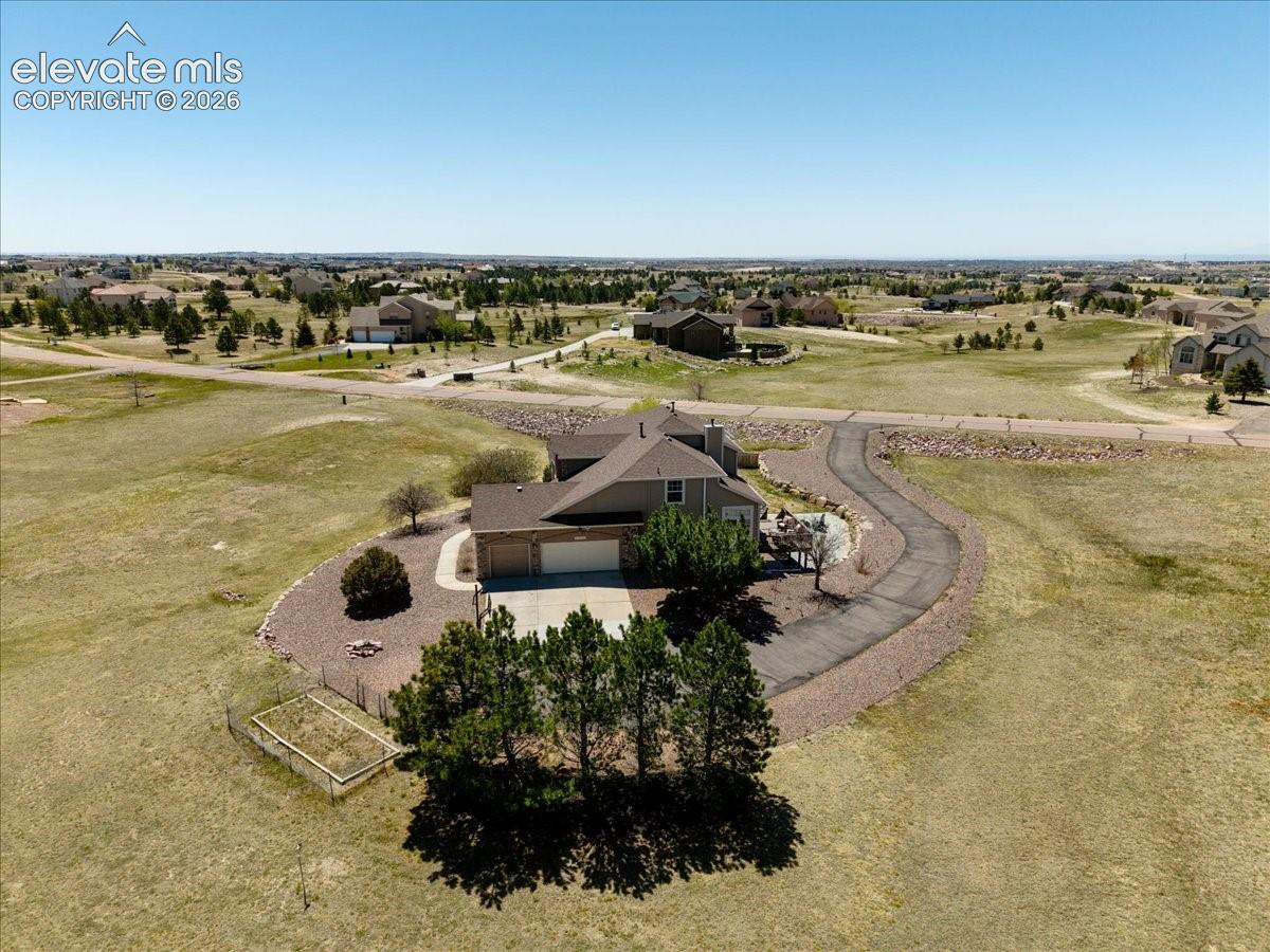 Ranch-style home with an attached 3-car garage, a long winding driveway, and surrounding natural landscaping