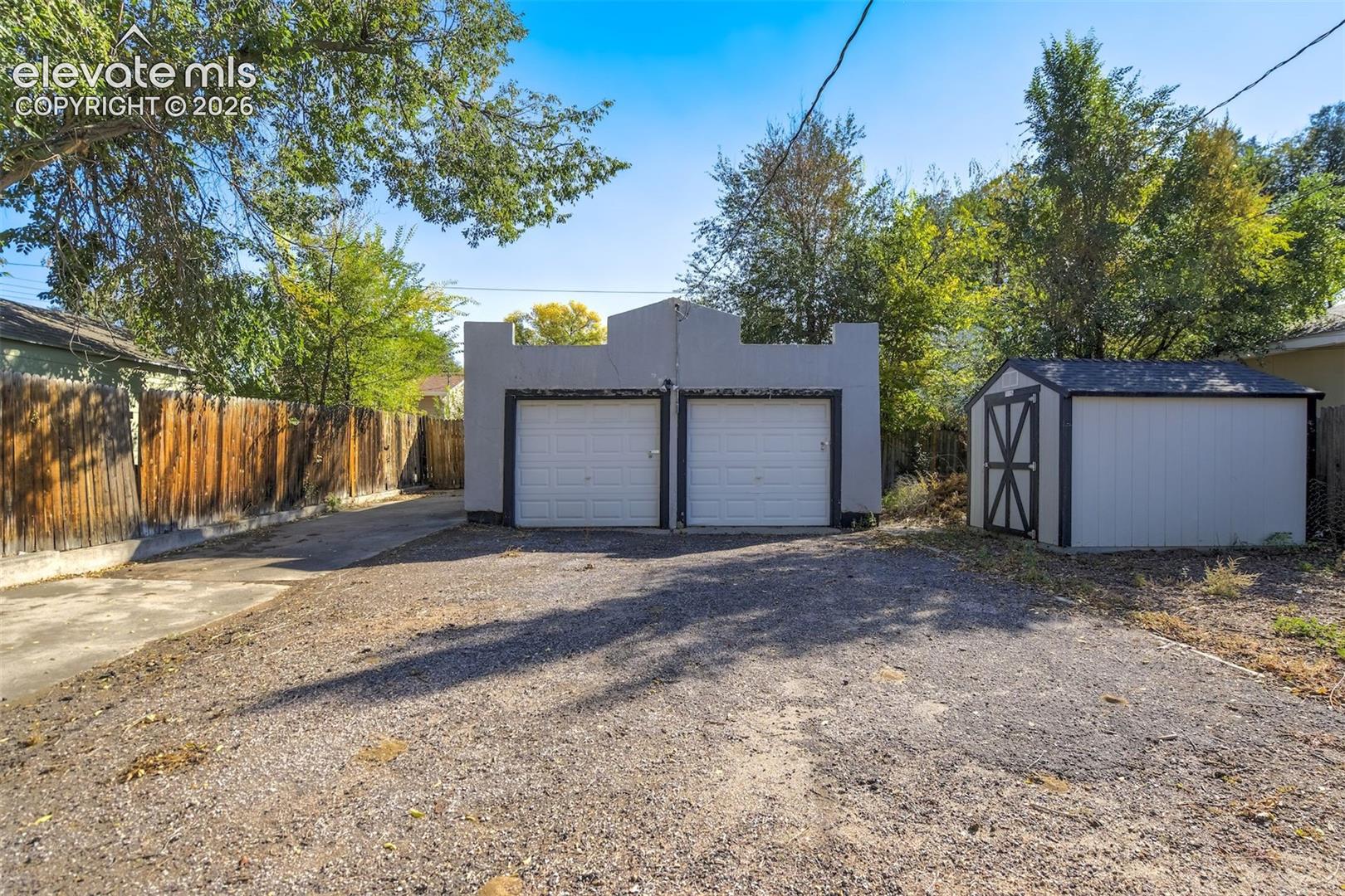 Detached two-car garage featuring a parapet roofline, two roll-up doors, and an attached storage shed