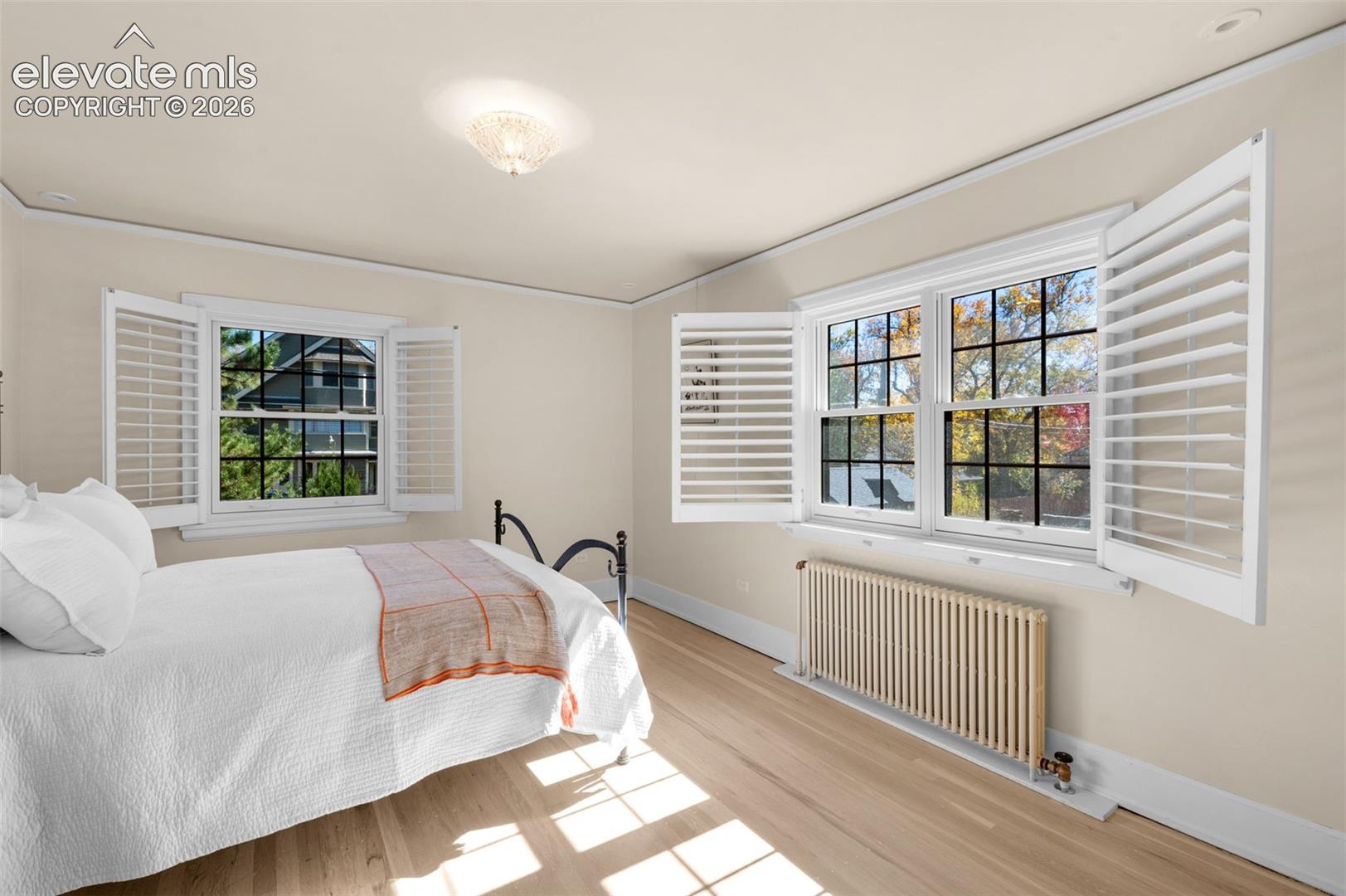 Hardwood flooring, multi-pane windows with white plantation shutters, and a vertical fin radiator