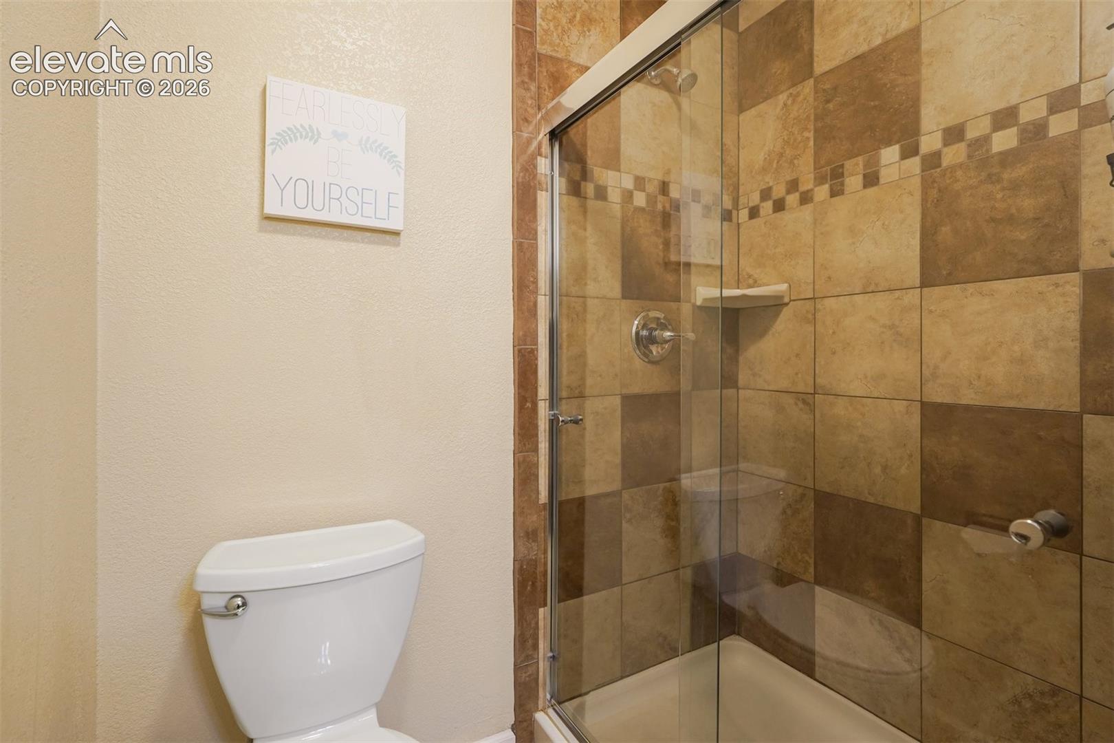 Tiled shower enclosure with a glass door, checkerboard tile pattern, and an integrated corner shelf