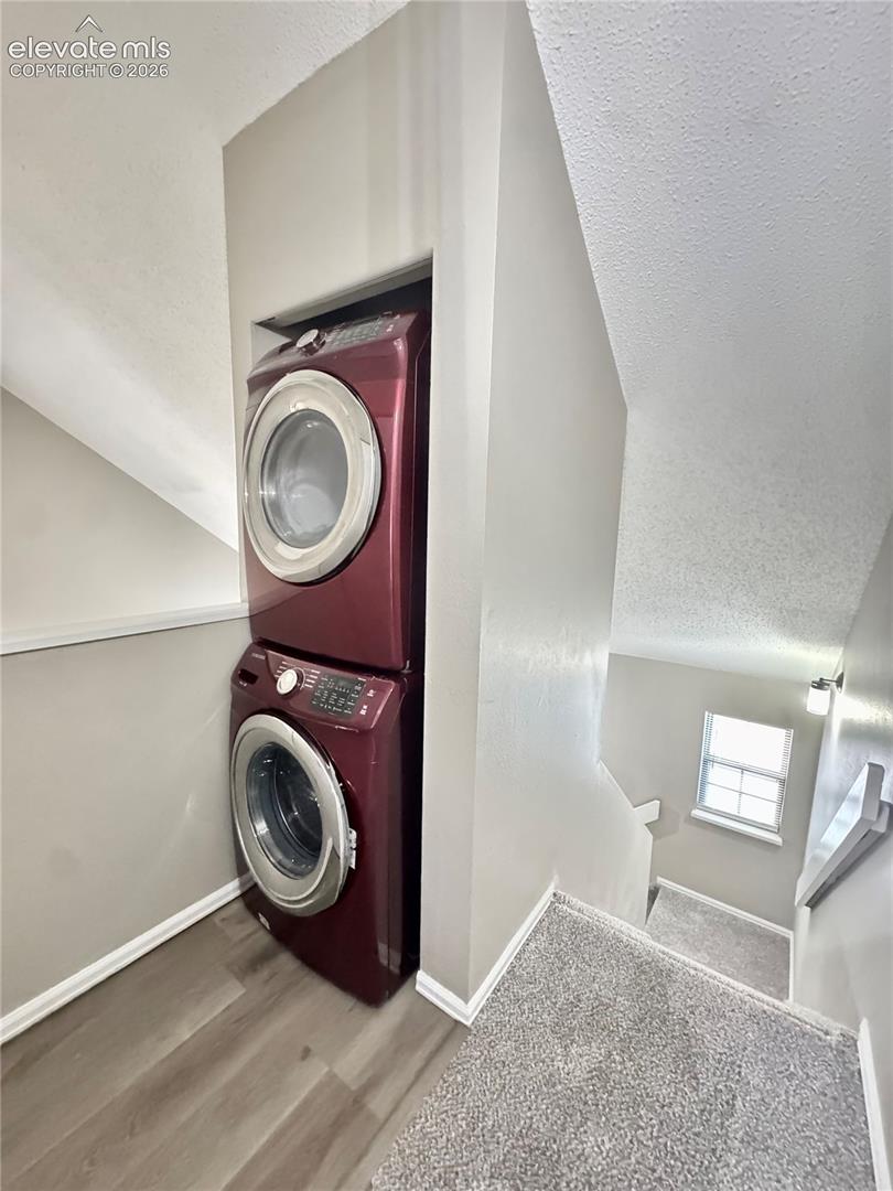 Built-in stacked laundry area with wood-finish flooring, neutral wall tones, carpeted stairs, and windowed stairwell lighting