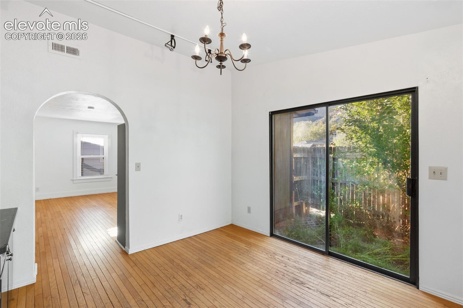 Interior space featuring wood-finish flooring, a decorative metal chandelier, an arched doorway, and a large sliding glass door