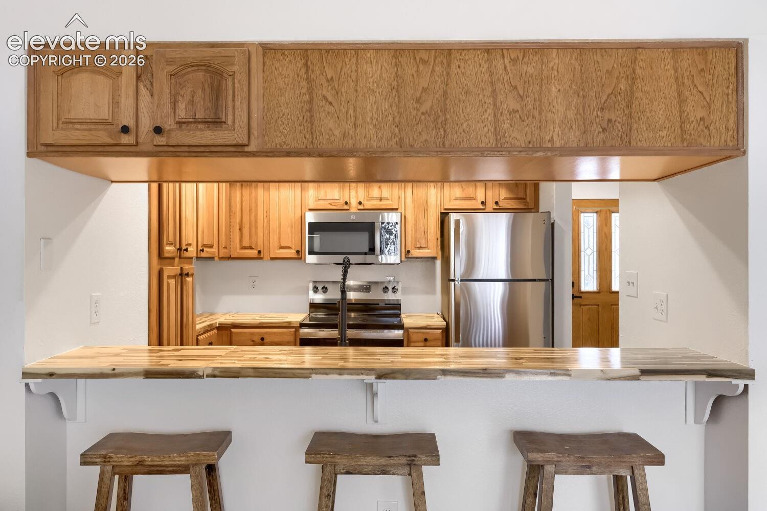 Kitchen featuring a wood-finish breakfast bar, light wood cabinetry, stainless steel appliances, and an over-the-range microwave