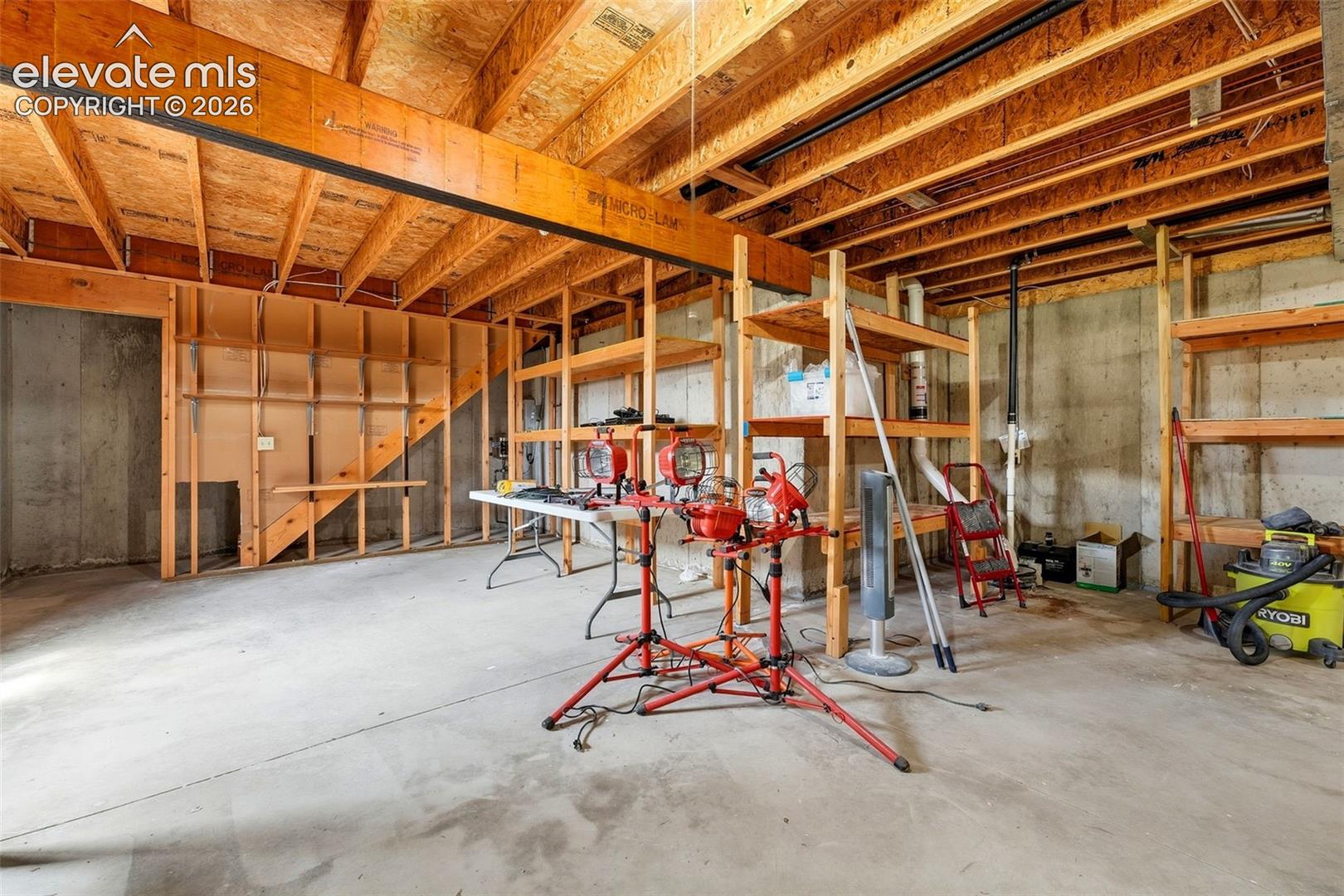 Unfinished basement space with exposed concrete walls, exposed ceiling joists, wood framing, and a concrete floor