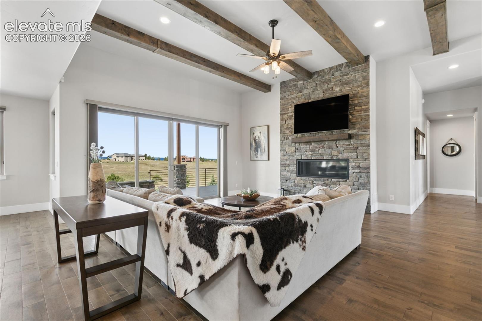 Living area with wood-finish flooring, exposed ceiling beams, and a stone-clad fireplace with a built-in linear firebox