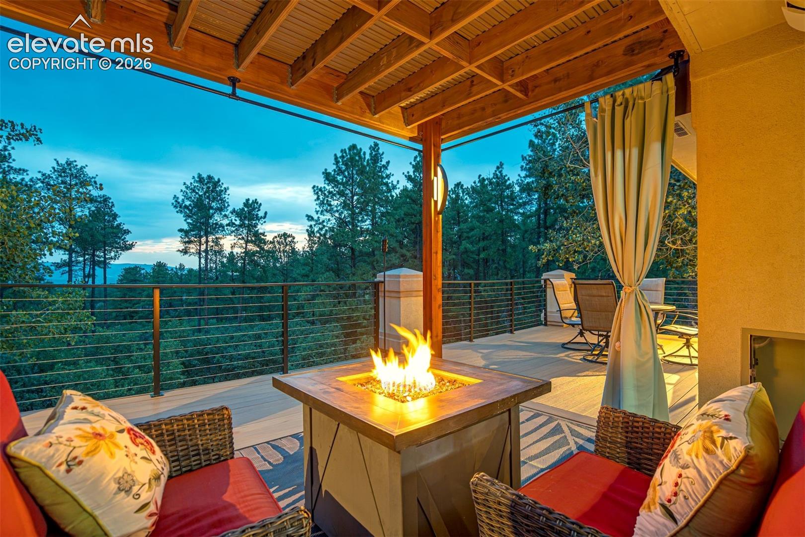 Covered outdoor deck featuring a wooden beam ceiling, a built-in fire pit, and metal cable railings