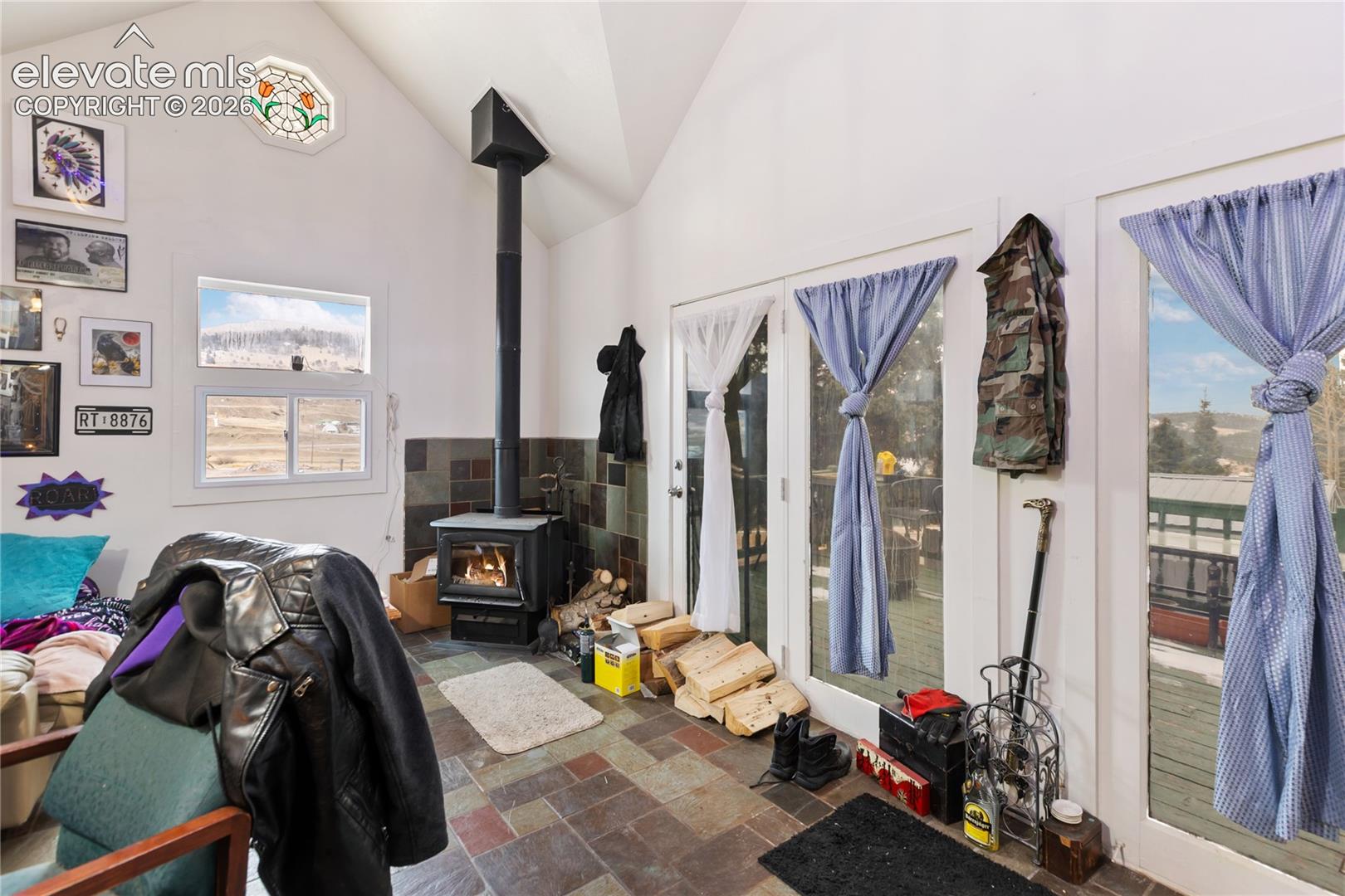 Vaulted ceiling with stained-glass accent window, slate-tile flooring, and freestanding wood-burning stove with a tiled surround
