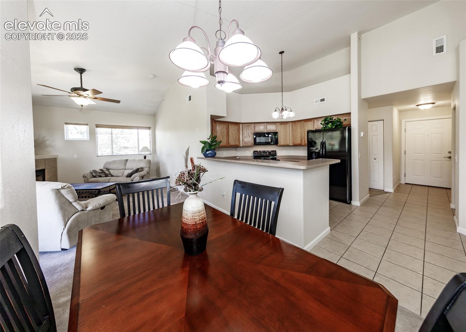Open-concept interior featuring vaulted ceilings, tile flooring, kitchen peninsula, wood-finish cabinetry, and decorative multi-light chandeliers