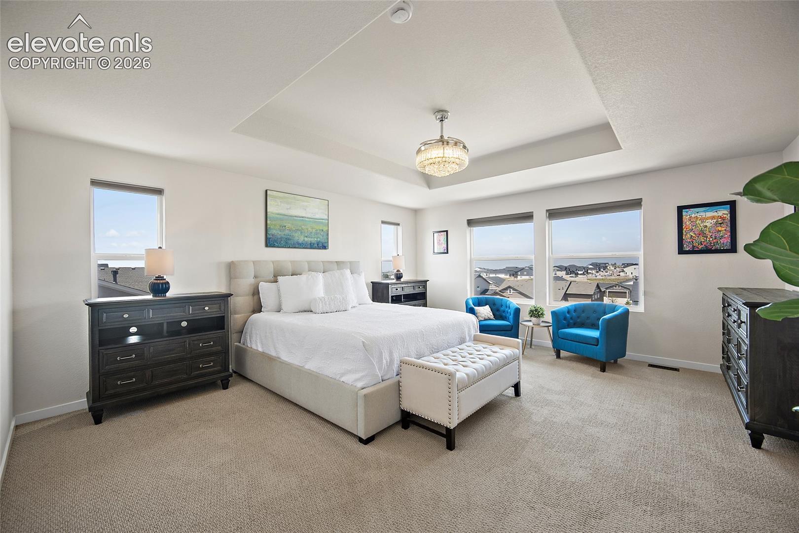 Recessed ceiling with a central chandelier, multiple windows, and light-toned wall finishes