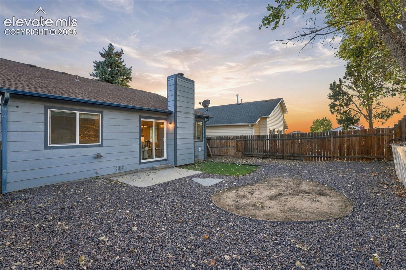 Exterior features include lap siding, a chimney with vertical cladding, a concrete patio, and a wood privacy fence