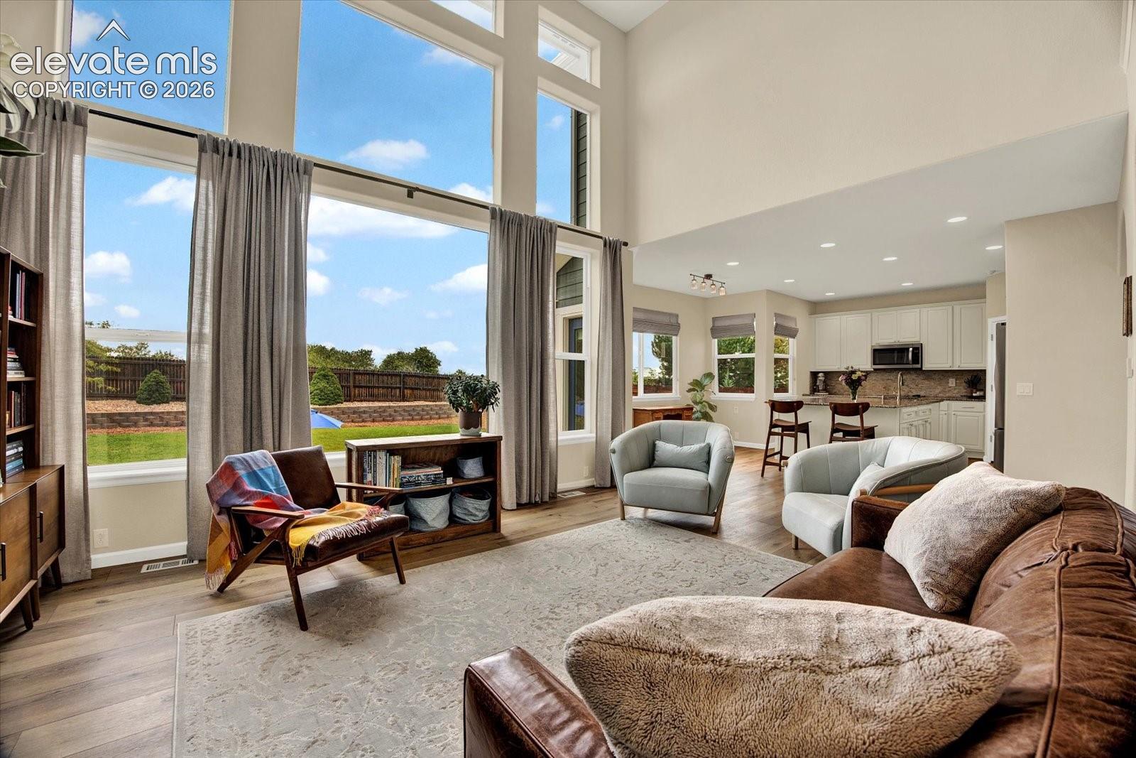Open-concept living area featuring floor-to-ceiling windows, soaring vaulted ceilings, recessed lighting, and wood-finish flooring