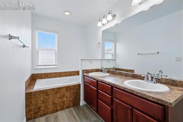 Full bath with wood finished floors, a garden tub, and double vanity