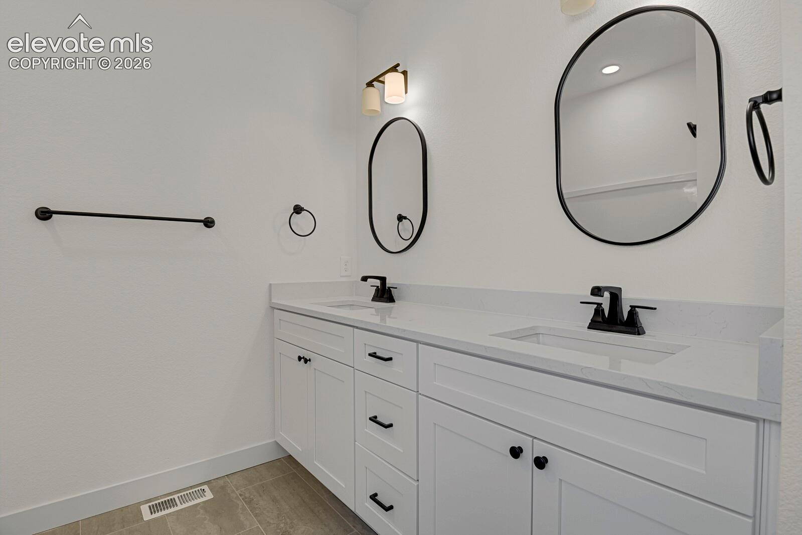 Dual-sink vanity featuring white cabinetry, solid-surface countertops, matte black hardware, dual oval mirrors, and wall-mounted light fixtures