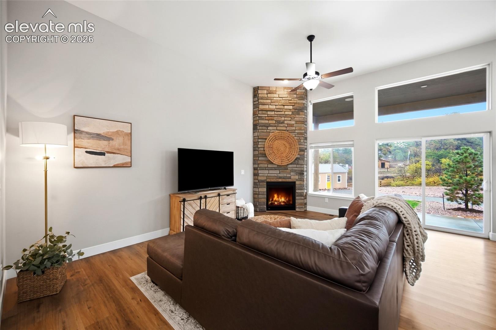Living area featuring soaring ceilings, a corner fireplace with stone veneer cladding, wood-finish flooring, and expansive windows with transom glass