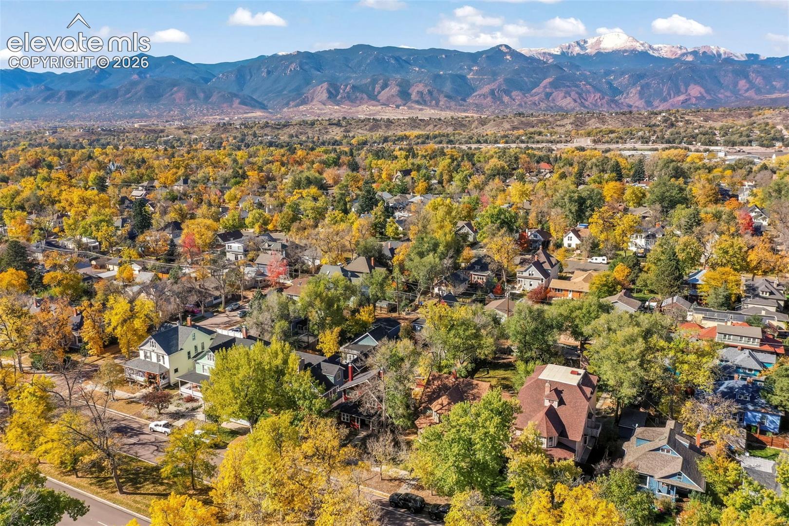 Aerial perspective featuring a mature residential landscape, abundant deciduous trees, and a prominent mountain range backdrop