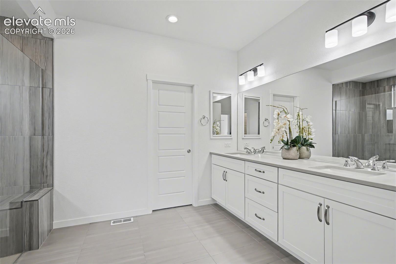 Bathroom featuring double vanity, a tile shower, and light tile patterned flooring