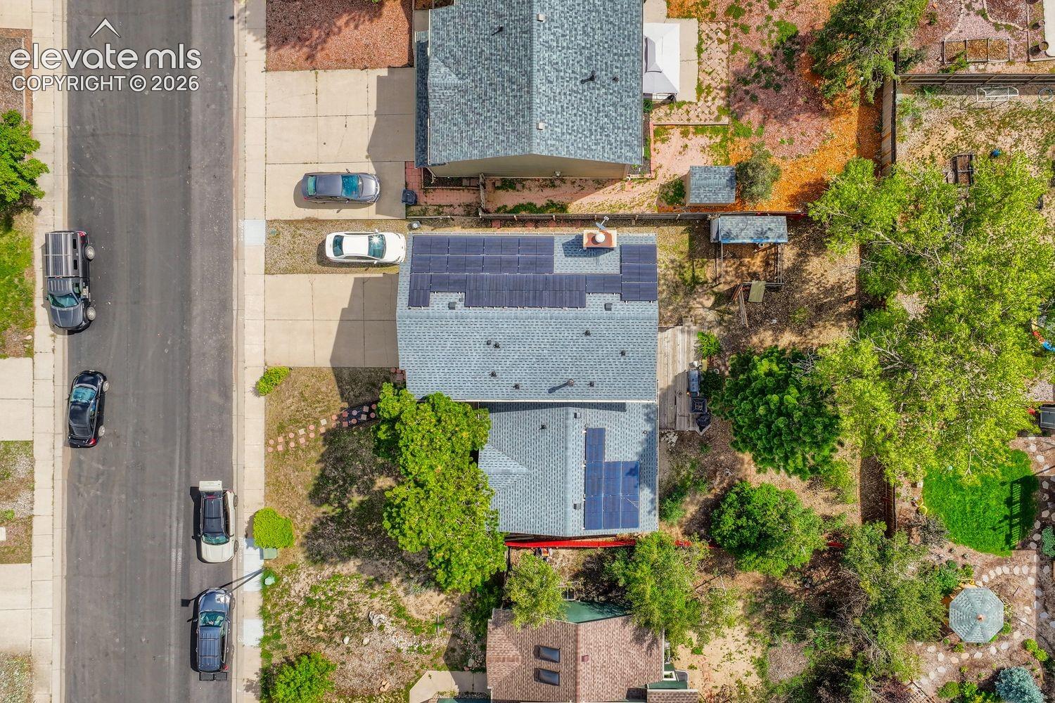 Residential property featuring a shingled roof, solar panel installations, a paved driveway, and mature trees