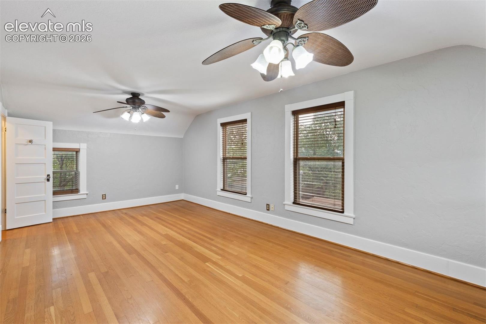 Primary bedroom with wood floor, ceiling fans, and walk in closet
