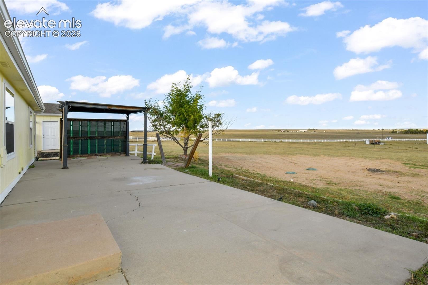 Expansive concrete patio featuring a black metal pergola with privacy screening