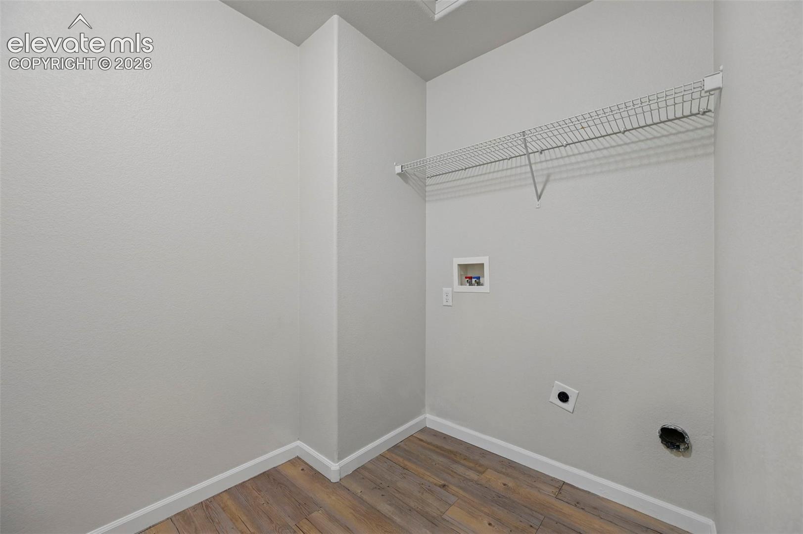 Dedicated laundry area featuring wood-finish flooring, light gray walls, and white baseboards
