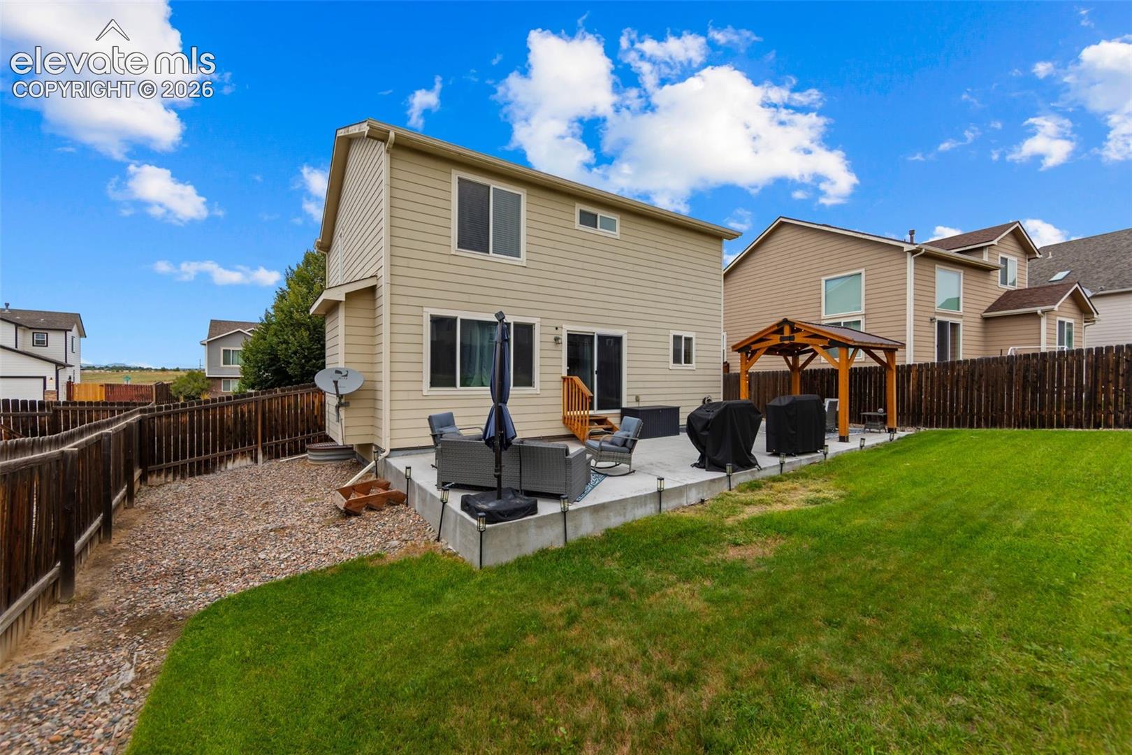 Expansive backyard featuring a manicured lawn, concrete patio, and a wood gazebo