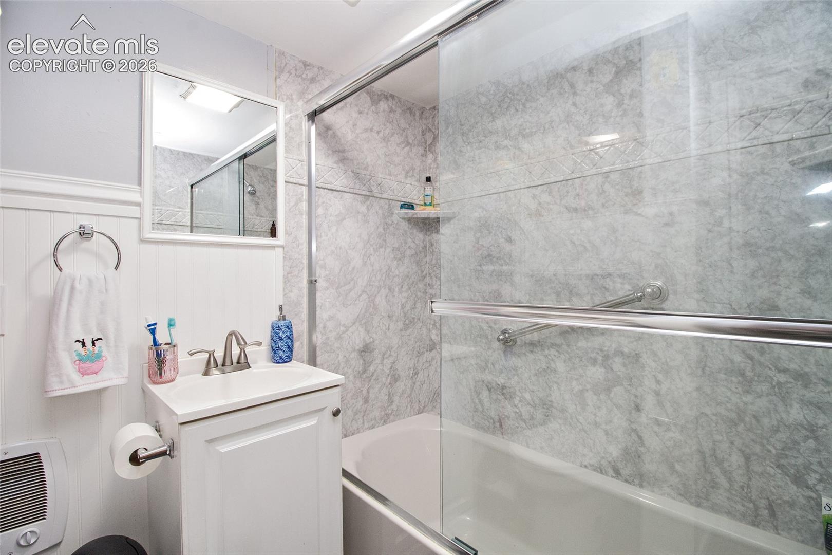 Bathroom featuring a shower-tub combination with glass sliding doors, stone-pattern wall surrounds, a white pedestal-style vanity, and a wall-mounted mirror