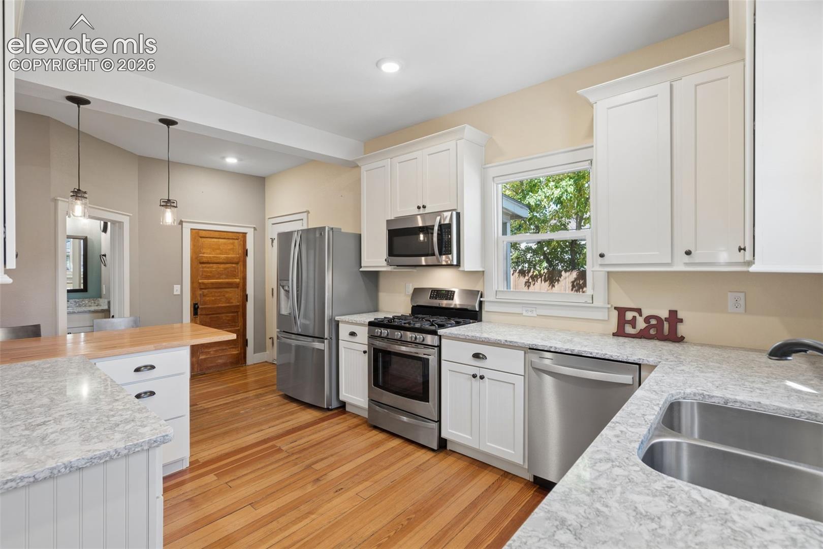 Kitchen featuring white shaker-style cabinetry, granite countertops, stainless steel appliances, wood flooring, and a breakfast bar with a butcher block countertop