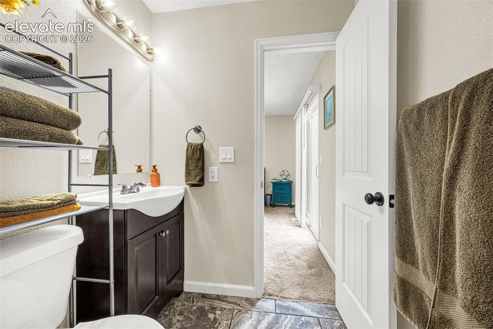 Dark-finish cabinetry featuring a curved integrated sink, stone-finish tile flooring, wall-mounted vanity mirror, and three-panel interior door with matte black hardware
