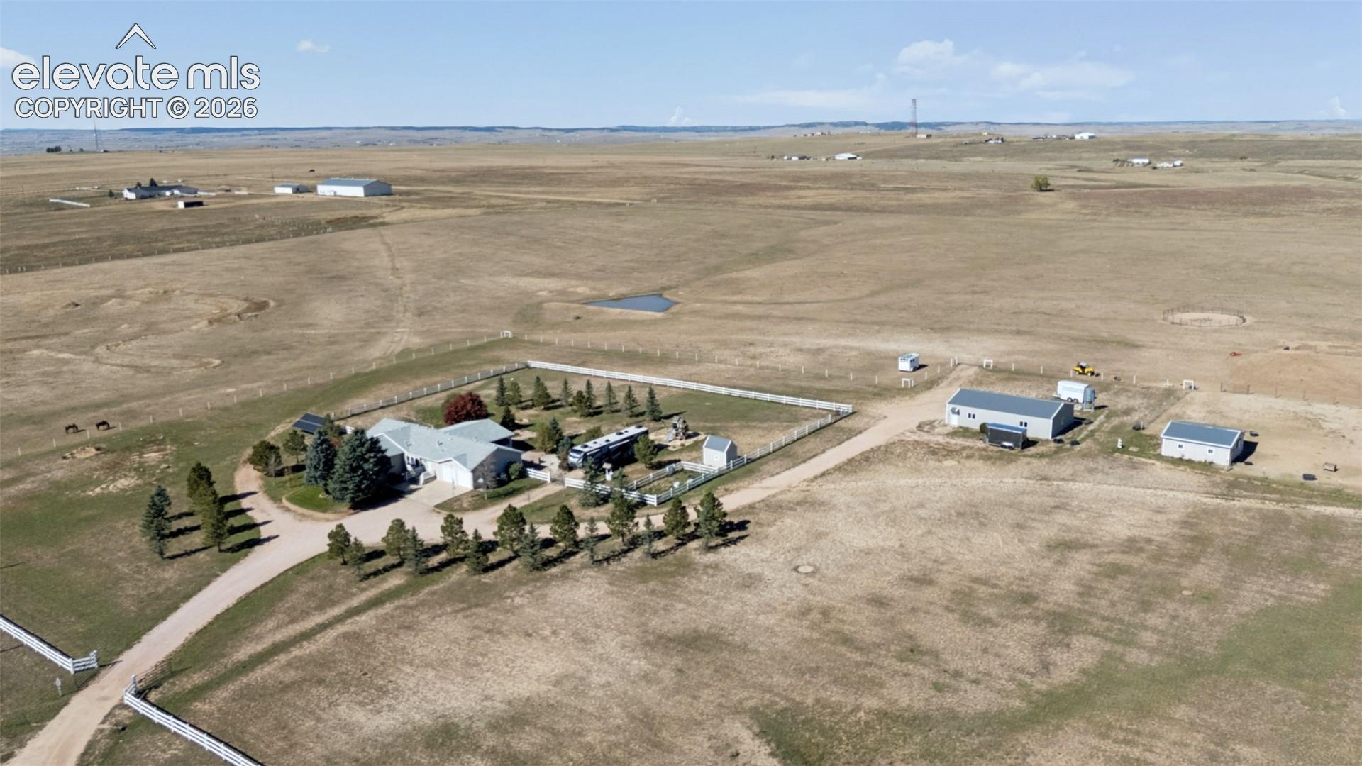 Aerial perspective of a sprawling property featuring a primary residence, two detached outbuildings, perimeter fencing, and an expansive acreage landscape