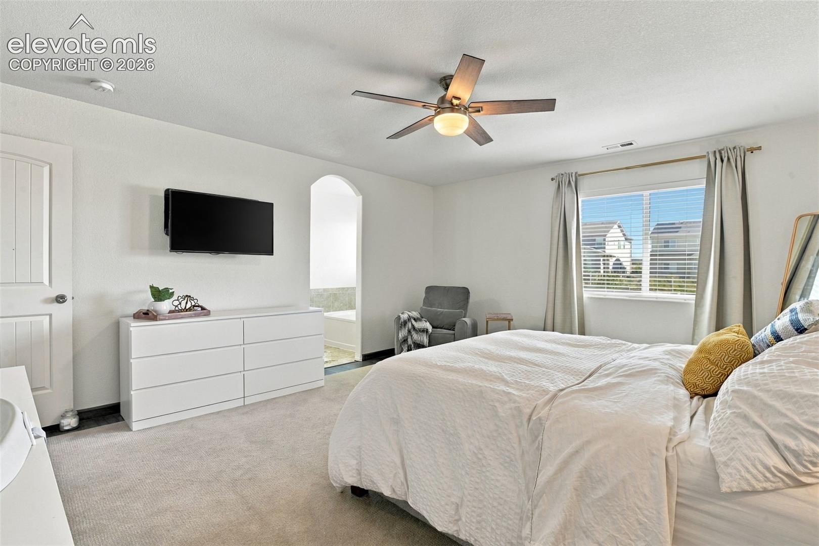 Carpeted flooring, ceiling fan with integrated lighting, window with blinds, and an arched doorway