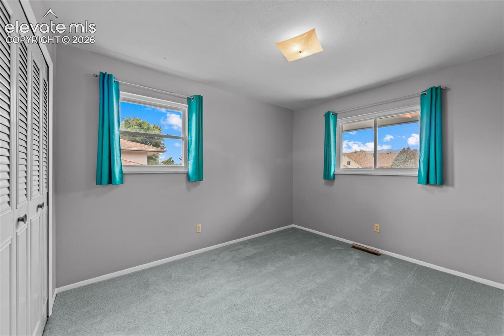 Louvered closet doors, wall-to-wall carpeting, and two windows providing natural light