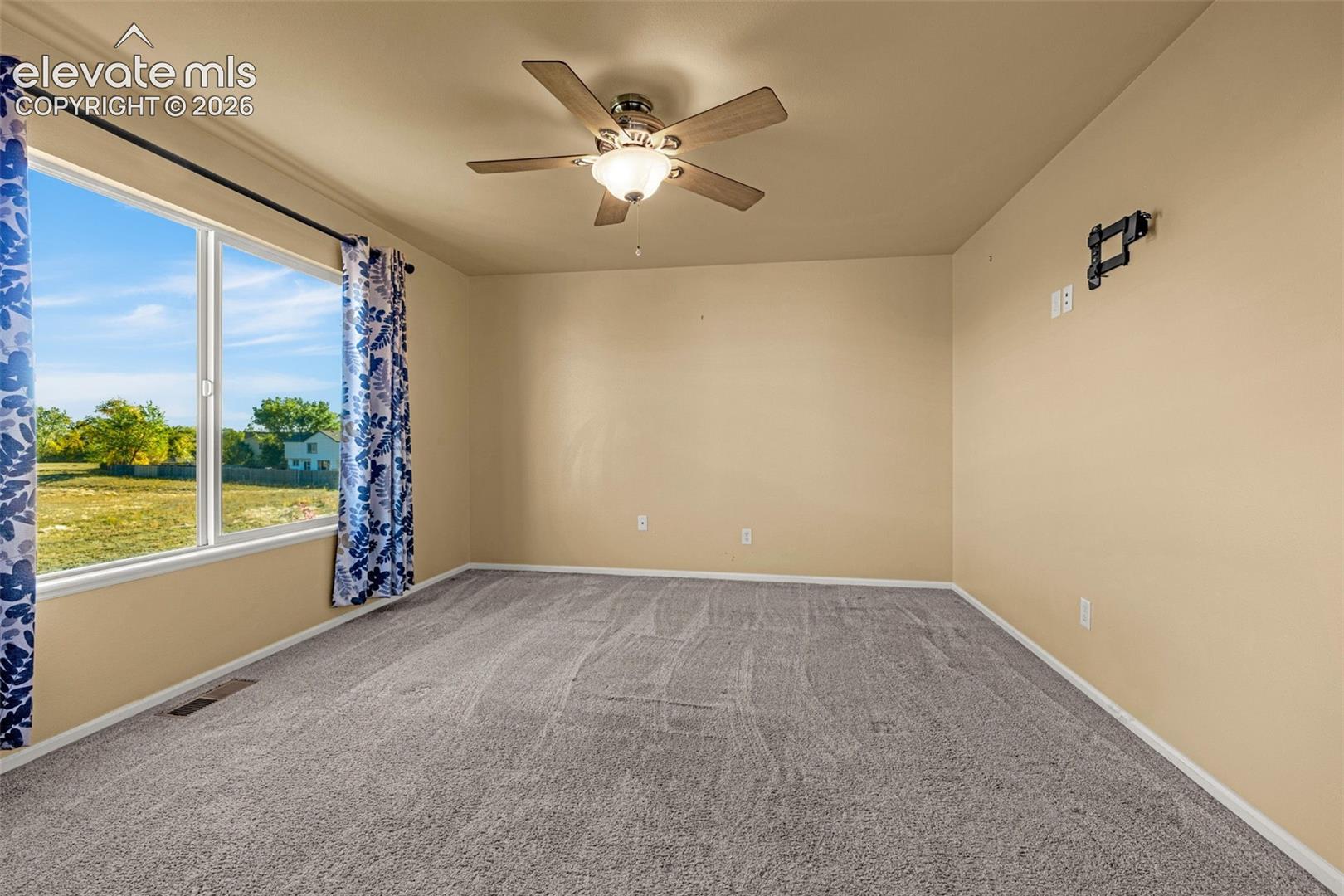 Neutral-toned room featuring a multi-blade ceiling fan with integrated lighting and expansive windows