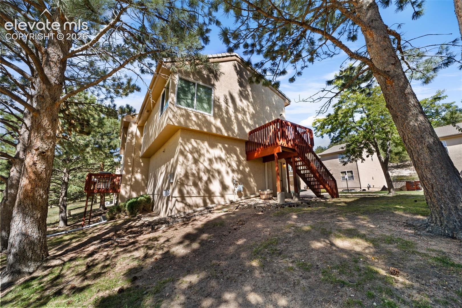 Stucco exterior featuring an elevated wood deck with railing and mature pine trees