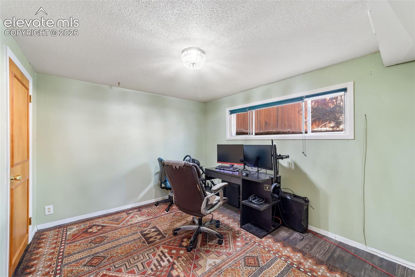 Room featuring wood-finish flooring, light green walls, a horizontal window with blinds, and a flush mount ceiling light